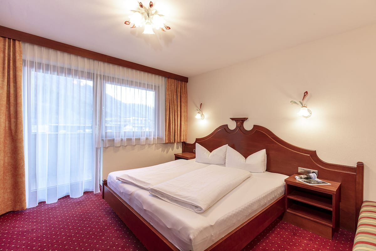 Ein Hotelzimmer mit einem großen Bett, einem Nachttisch aus Holz, einem kleinen Tisch und einem Fenster mit Vorhängen.
