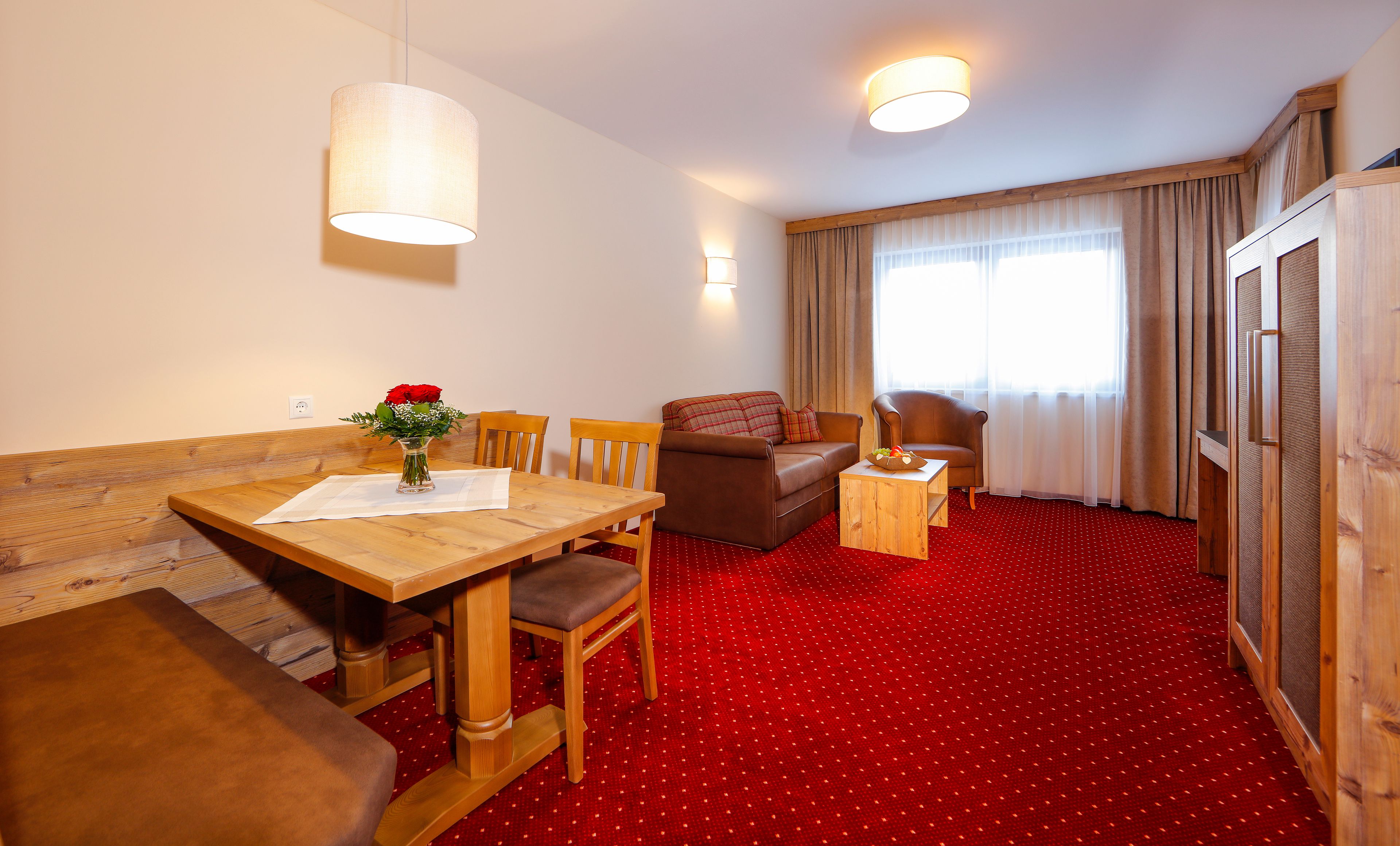 Ein Hotelzimmer mit einem Holztisch, einer Sitzecke, einem kleinen Beistelltisch und einem roten Teppichboden.