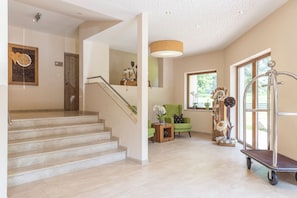 A staircase leading to a landing with a wooden door, a green armchair, and a decorative plant arrangement. - Panorama Appartements (Laengenfeld)