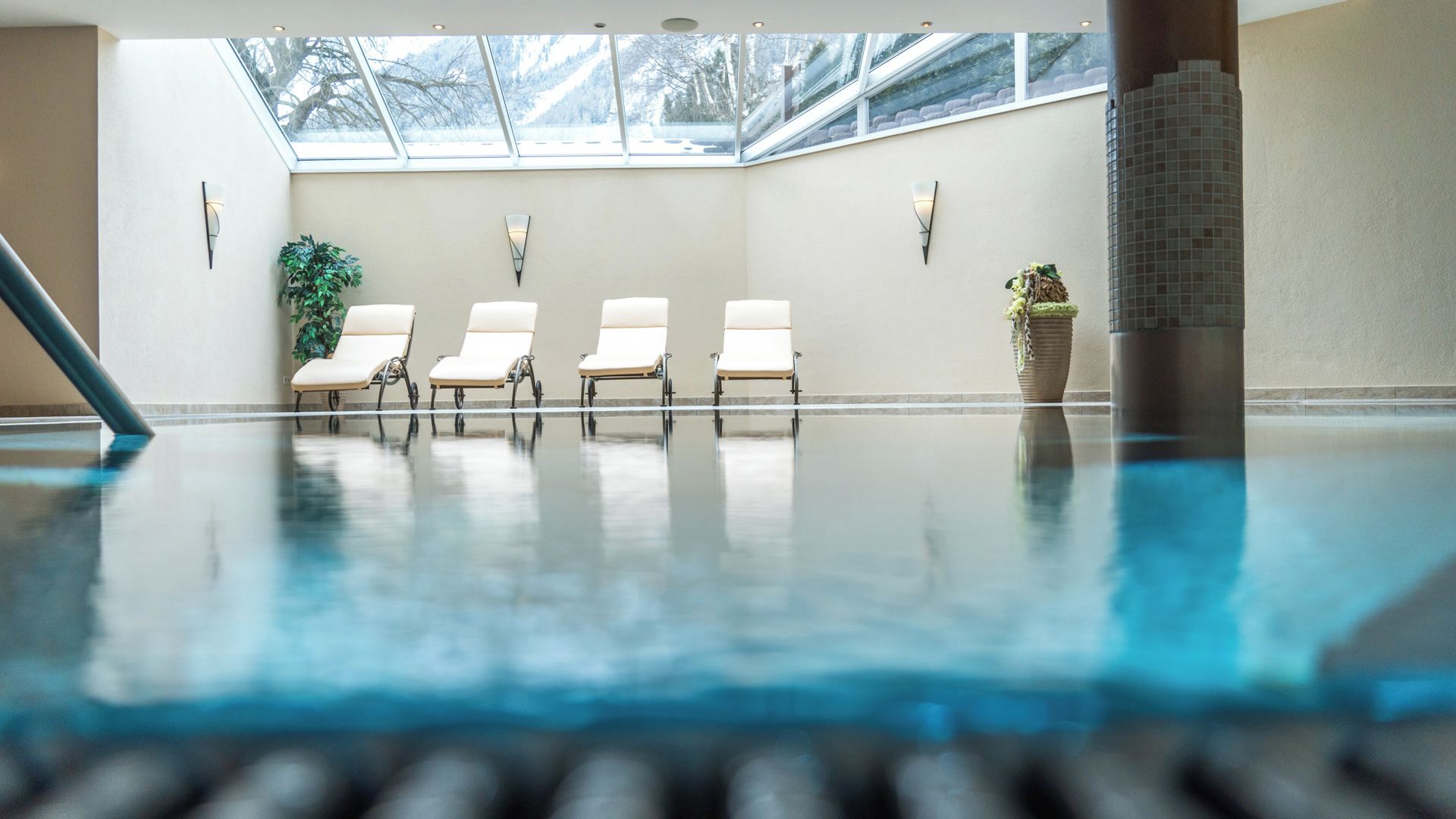 Piscina com quatro espreguiçadeiras e um vaso de planta.