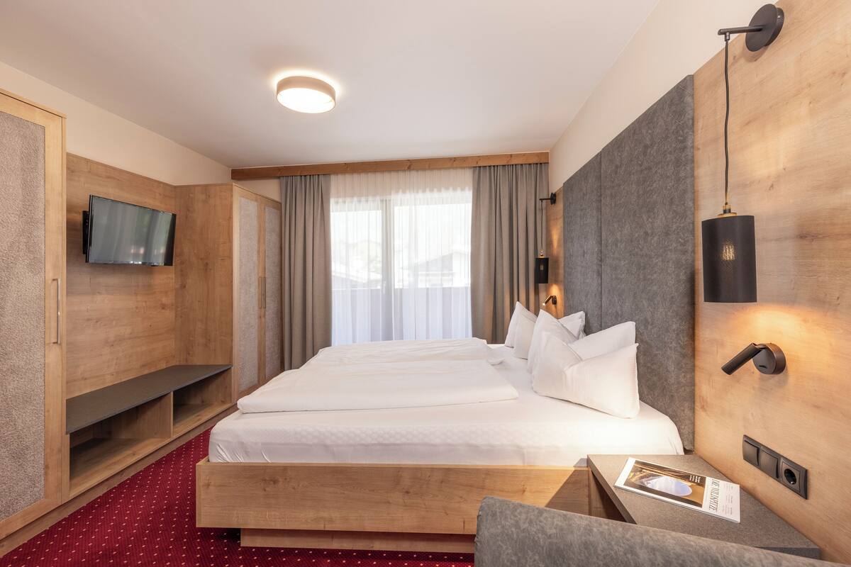 Ein Hotelzimmer mit einem großen Bett, einem an der Wand montierten Fernseher, einem Holzkopfteil und einem roten Teppich.