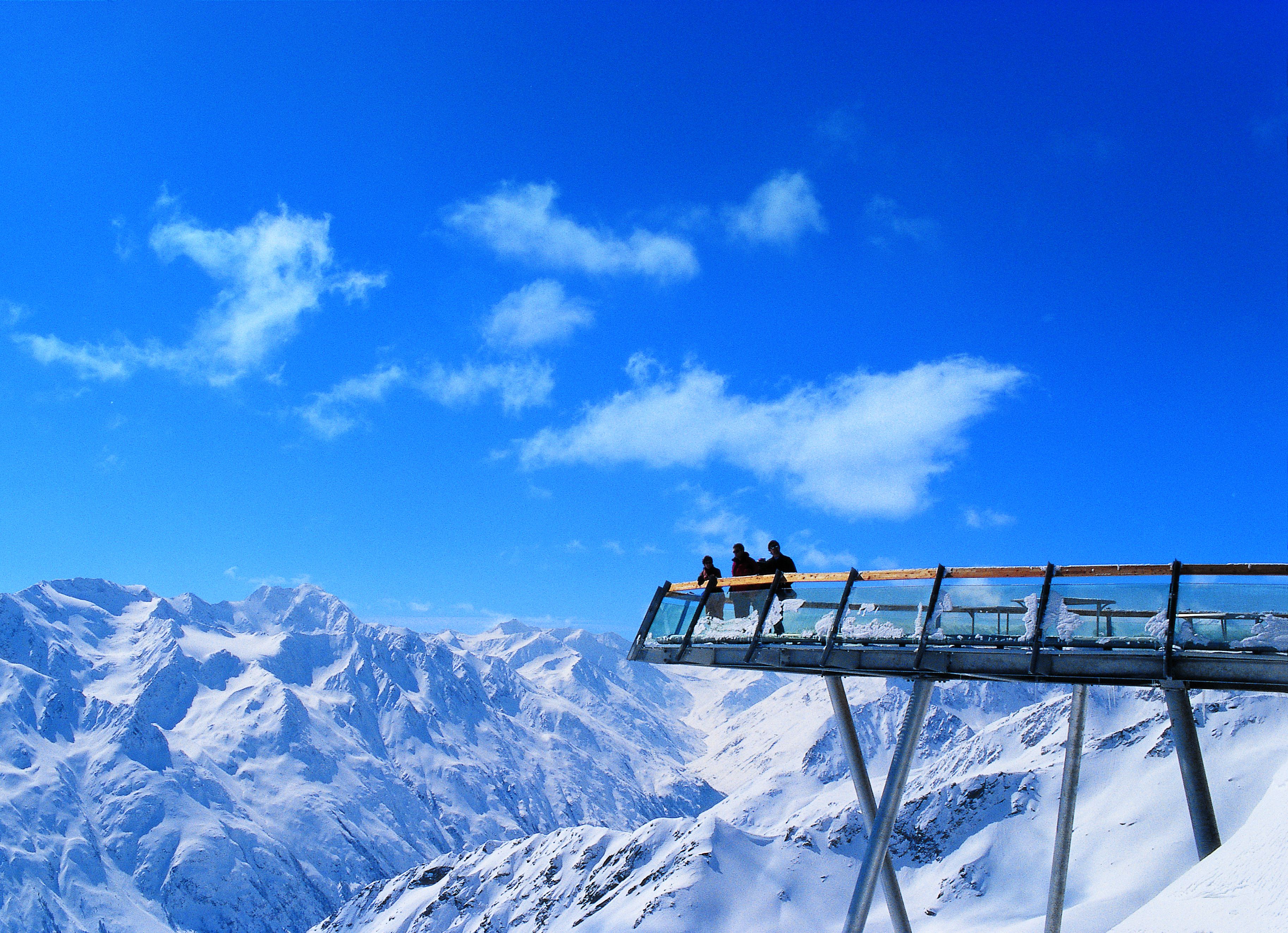 Un puente de cristal con soportes metálicos sobre un paisaje montañoso nevado.