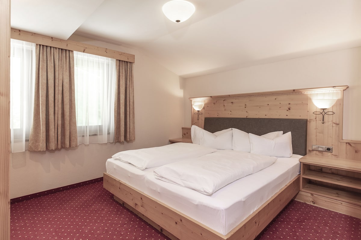 Ein Hotelzimmer mit einem Holzbett, einem Nachttisch, einer Lampe und einem Fenster mit Vorhängen.
