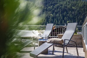 A balcony with two lounge chairs, a small table with a glass, and a view of a forested mountain. - Panorama Appartements (Laengenfeld)