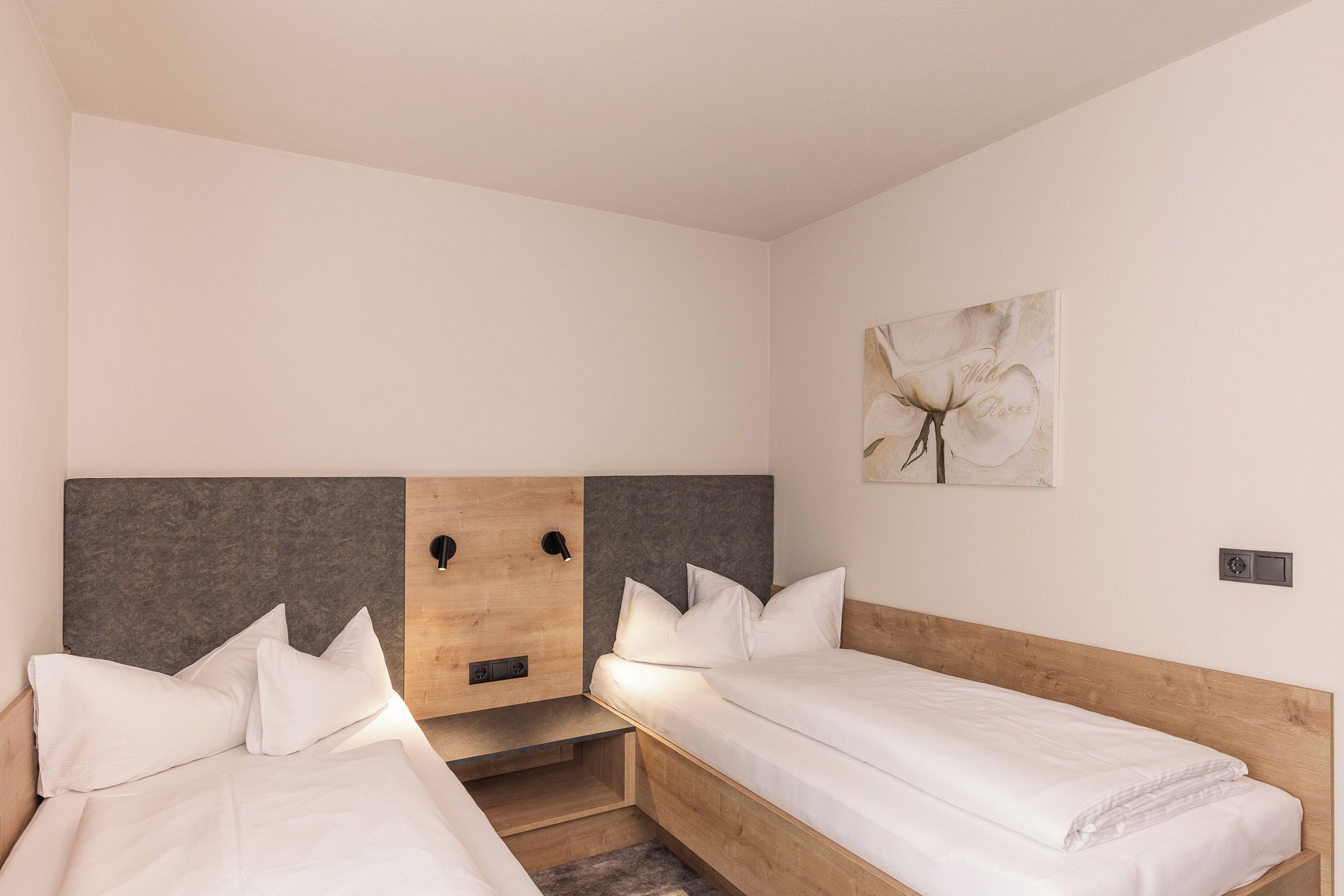 Une chambre d’hôtel avec deux lits simples, une tête de lit en bois, un mur d’accent de couleur grise et un tableau représentant une fleur.