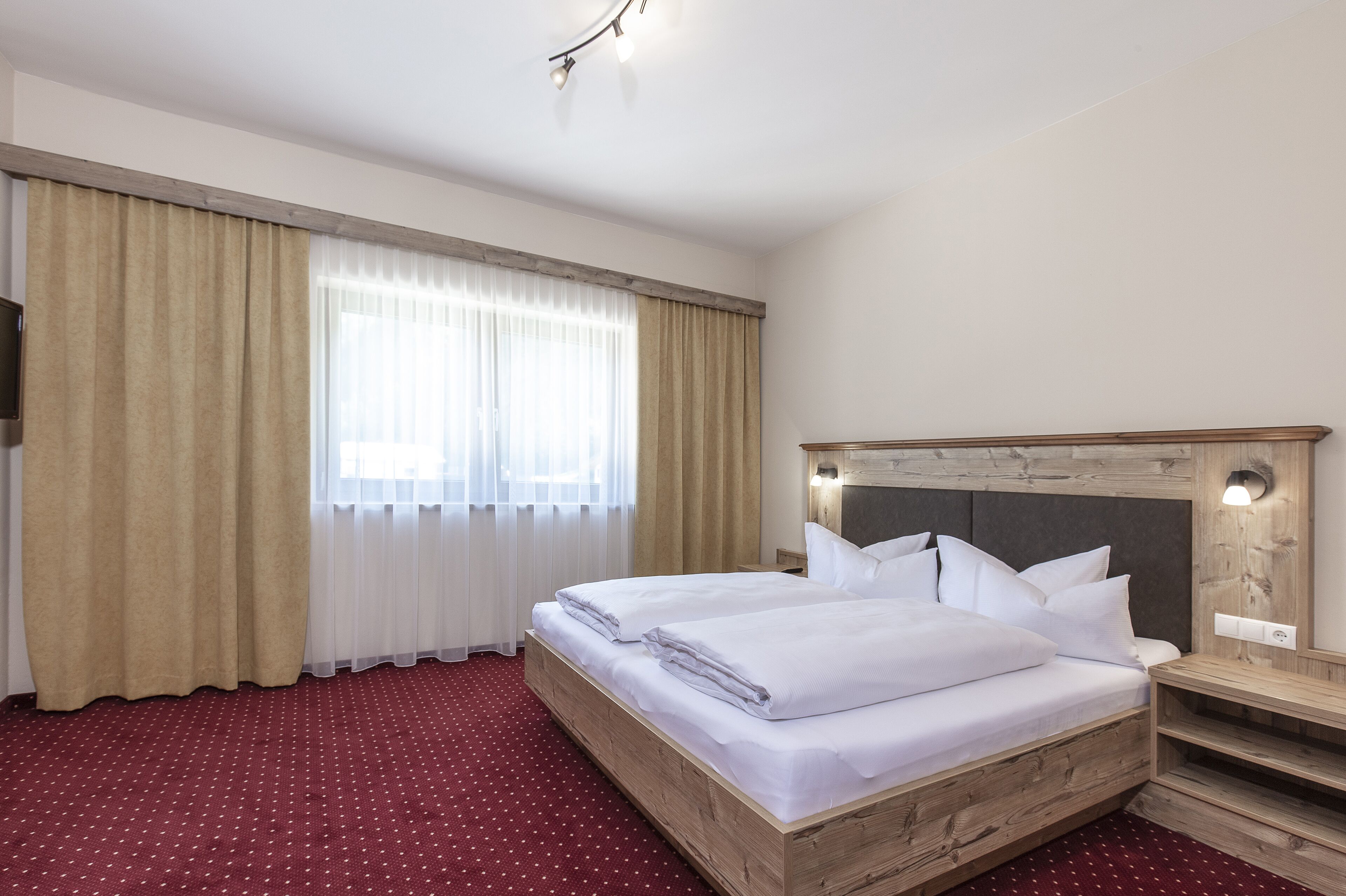 Een hotelkamer met een houten bed, een nachtkastje, een spiegel en een raam met gordijnen.