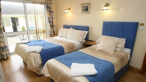 A hotel room with two beds, each with a blue headboard and beige bedding. There are two bedside tables with lamps, and a window with curtains. - Teach na Coiribe (Galway)