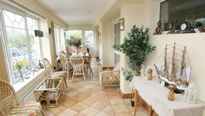 A sunlit room with wicker furniture, a dining table, and a ship model. - Teach na Coiribe (Galway)