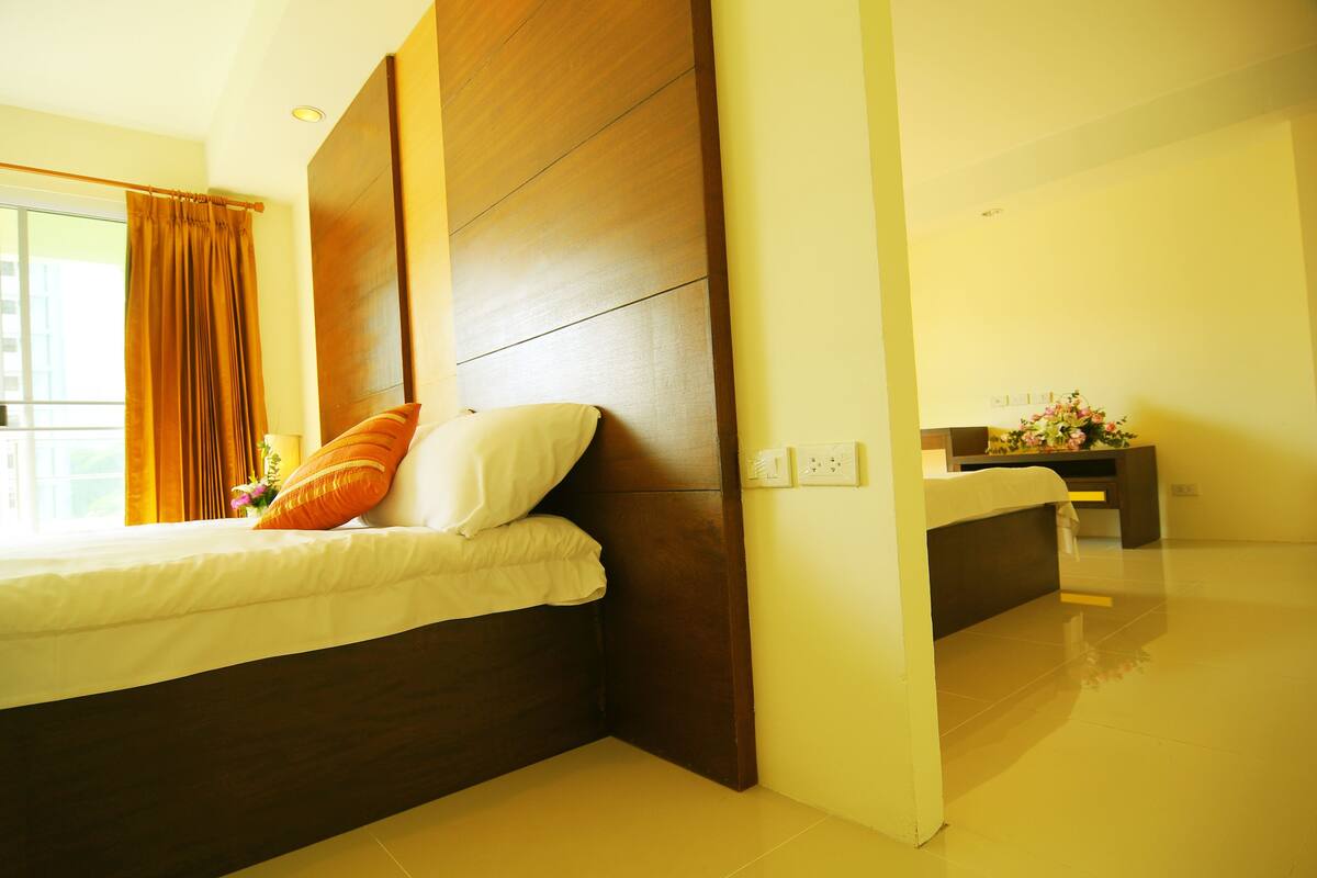 A modern hotel room with a large bed, wooden headboard, and a small bedside table with a vase of flowers.