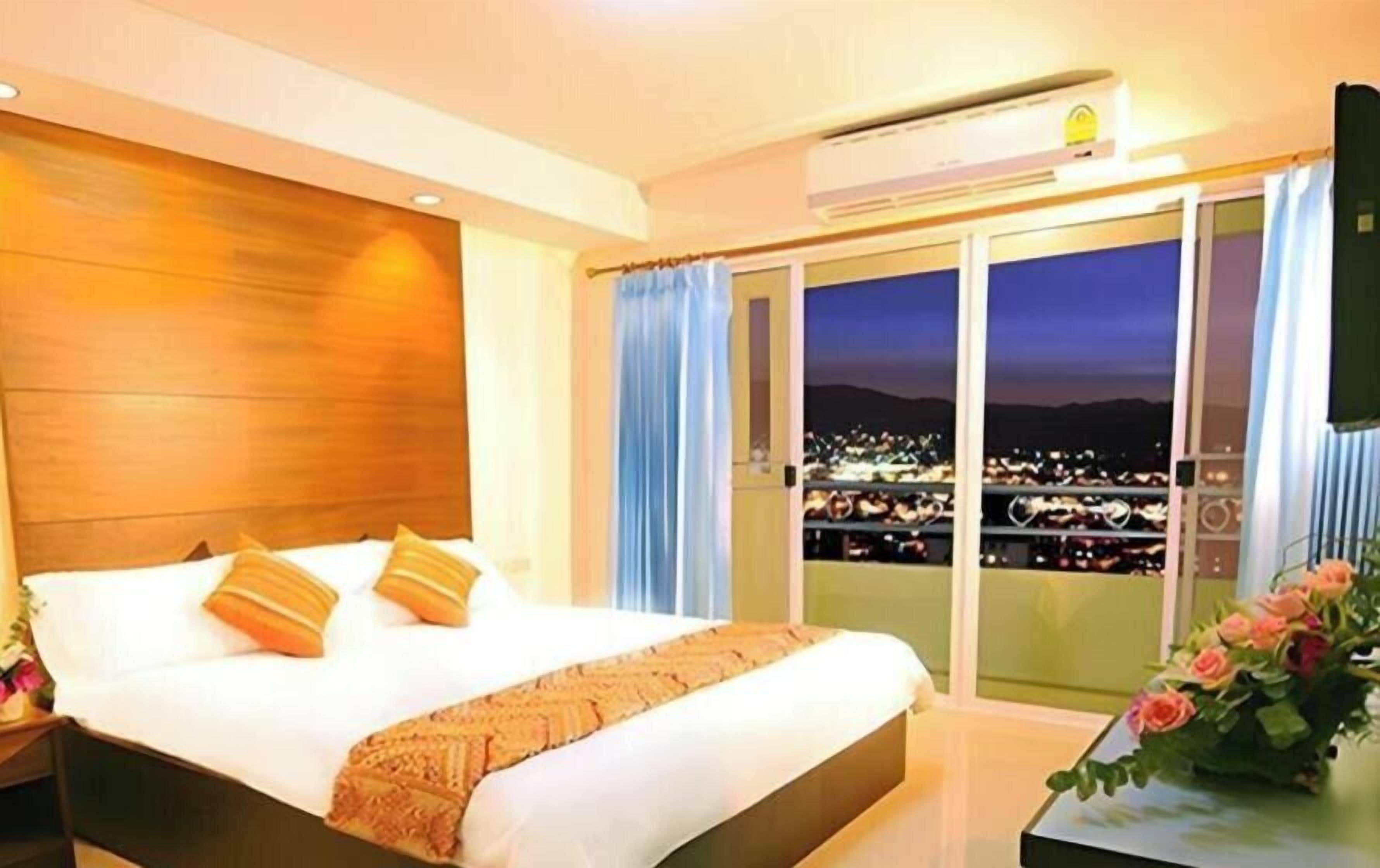 A hotel room with a large bed, a view of the city at night, and a balcony with curtains.