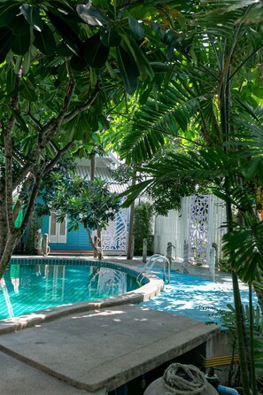 A swimming pool surrounded by lush greenery, with a decorative fence and a building in the background. - Deeden Pattaya Resort (Pattaya)