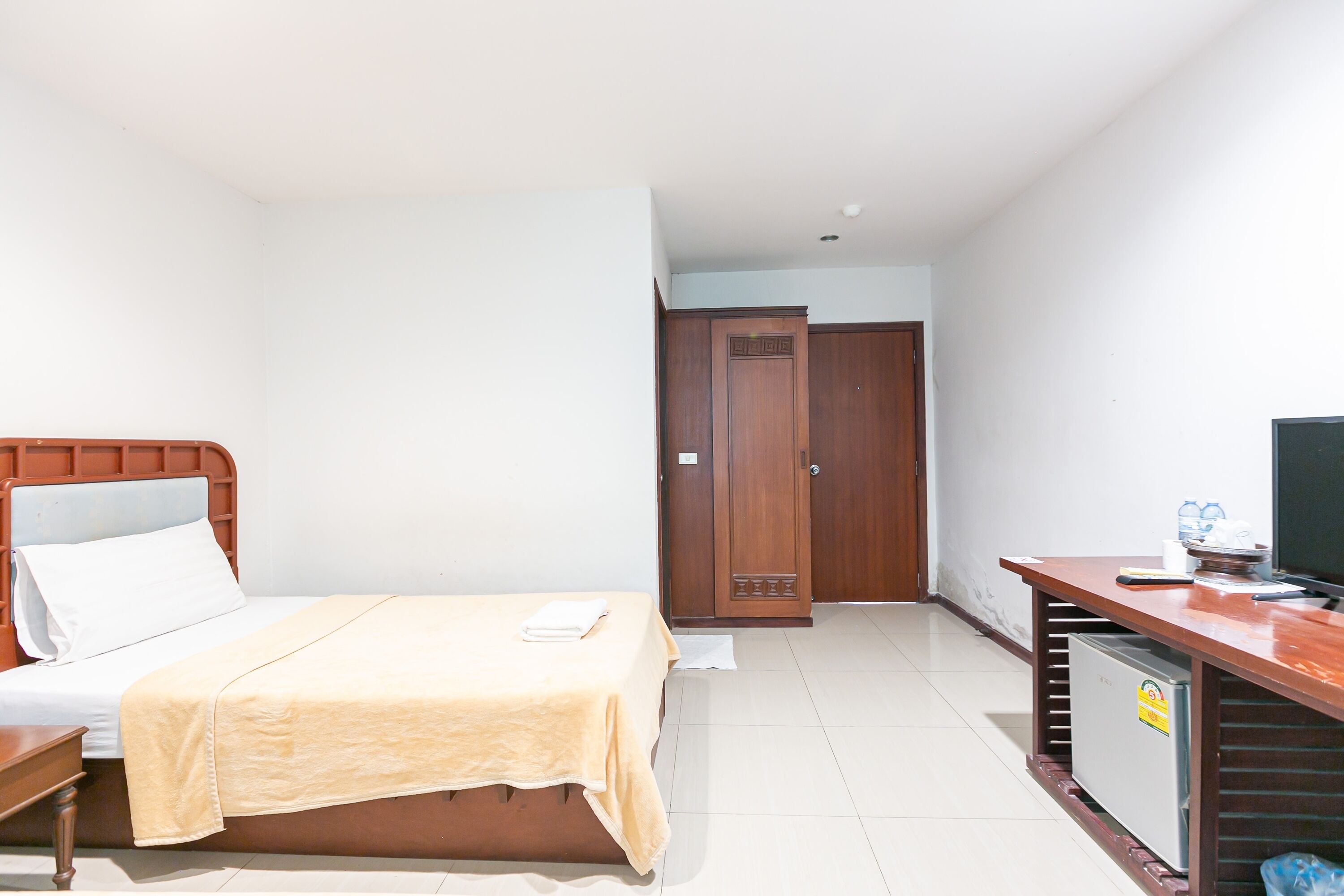 A hotel room with a bed, a desk with a computer, a television, and a small refrigerator.