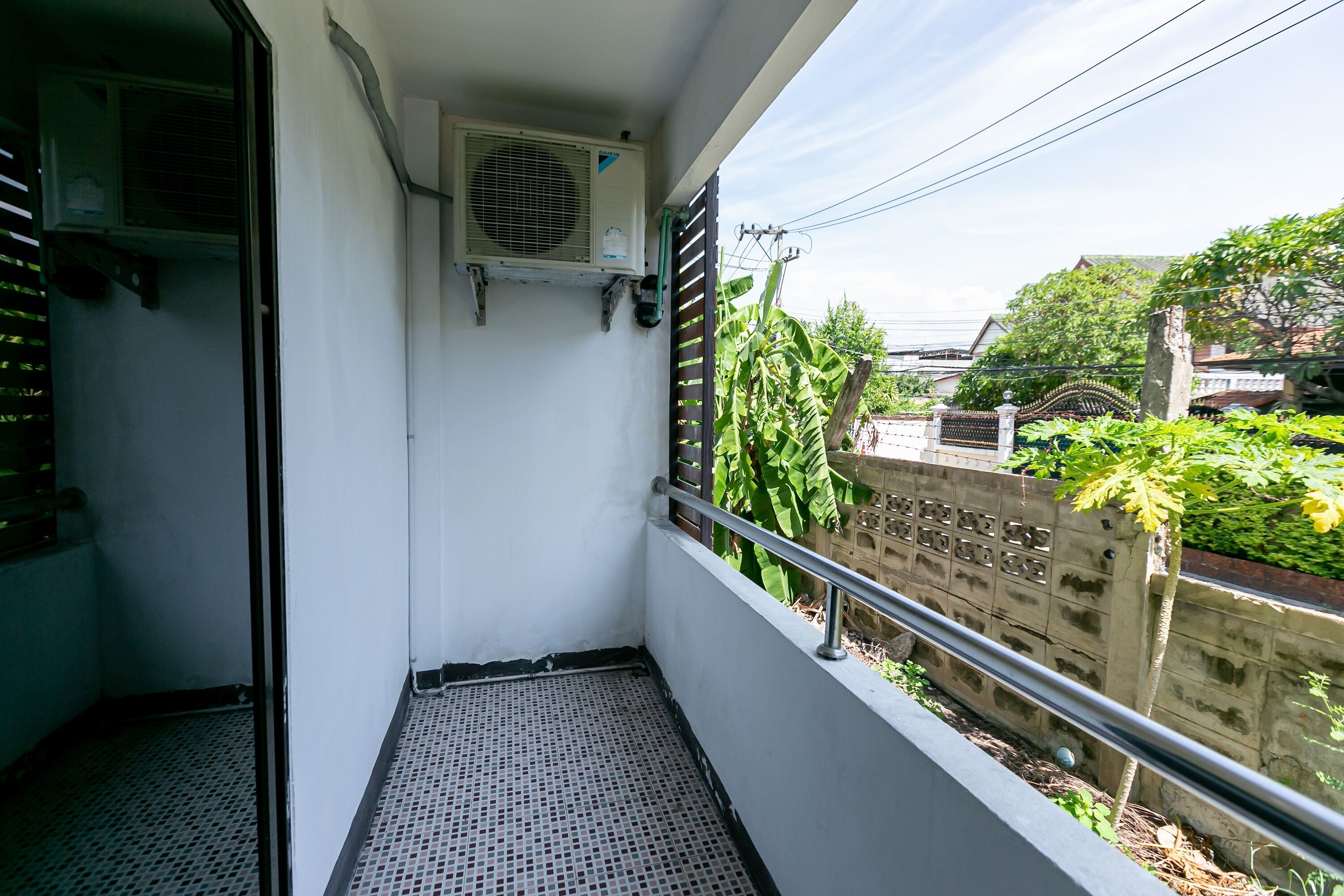 Un balcon doté d’une rambarde en métal, d’un mur blanc et d’un appareil de climatisation fixé au mur.