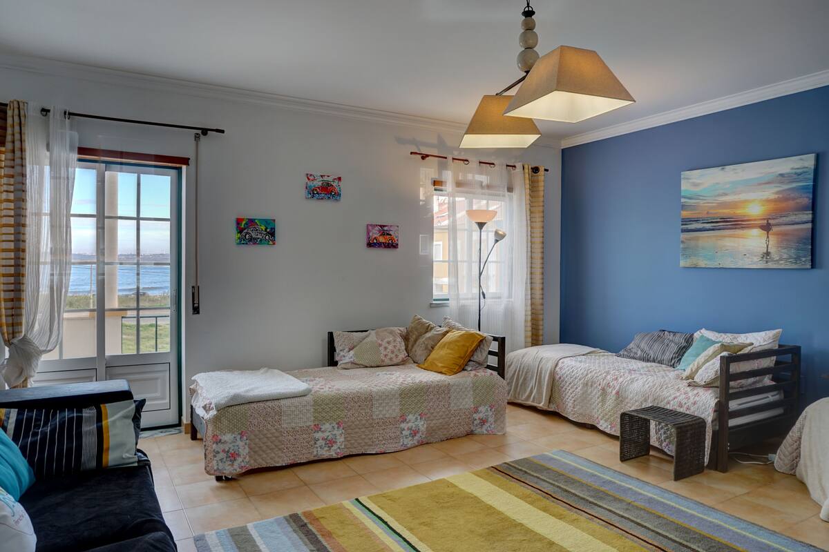 Un dormitorio con dos camas, una ventana con cortinas, una lámpara y un cuadro en la pared.