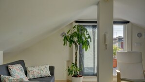 A modern living room with a grey sofa, a potted plant, and a white chair. - Peniche Surf Lodge - Hostel (Peniche)