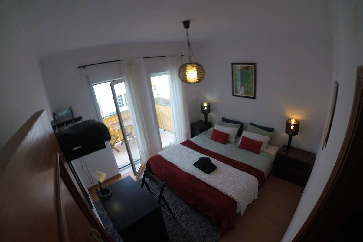 Un dormitorio con cama, mesitas de noche, un escritorio y un balcón.