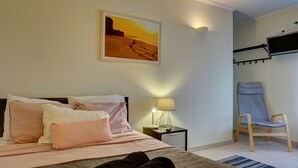 A bedroom with a bed, pillows, a nightstand with a lamp, a chair, and a wall-mounted TV. - Peniche Surf Lodge - Hostel (Peniche)