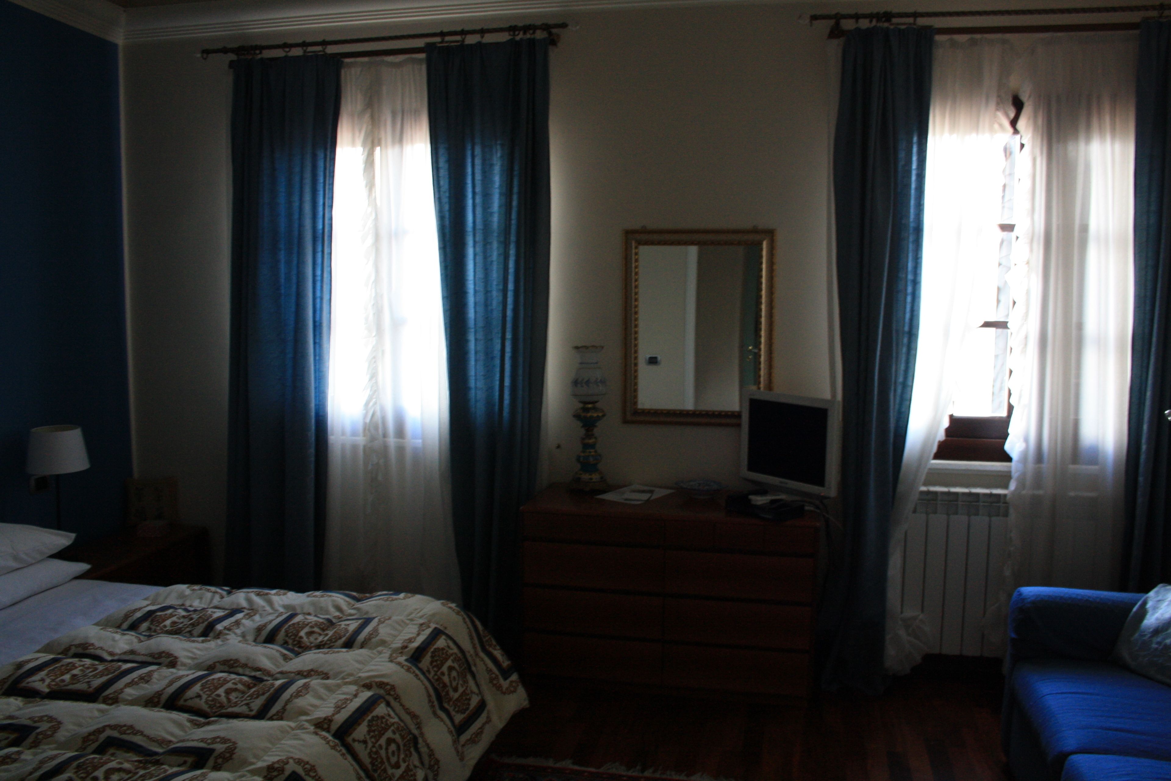 A hotel room with a bed, a dresser, a mirror, a TV, and a window with curtains.