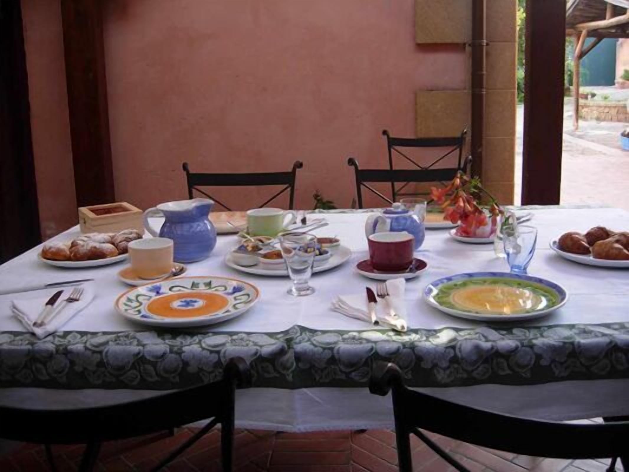 Una mesa lista para el desayuno, con platos, tazas y una tetera.