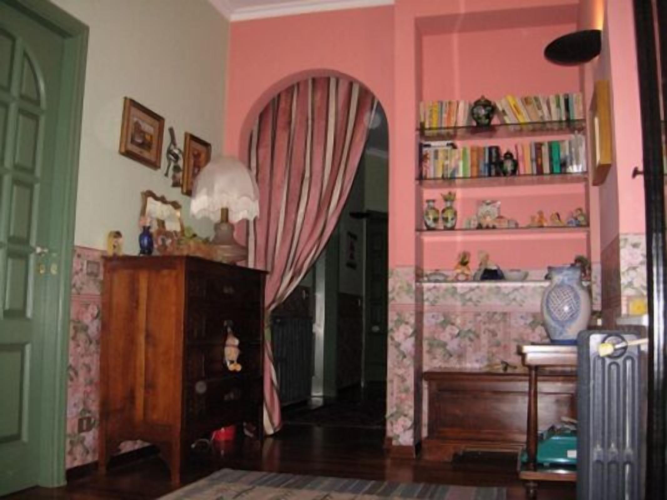Una stanza con un armadio in legno, una libreria con diversi oggetti e un termosifone.