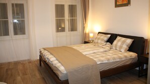 A bedroom with a bed, bedside tables, a window with curtains, and a wall-mounted painting. - Luxury Oldtown Apartments (Vienna)