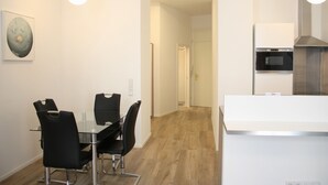 A modern kitchen with a built-in oven and a white countertop. There is a dining area with a glass table and black chairs. - Luxury Oldtown Apartments (Vienna)