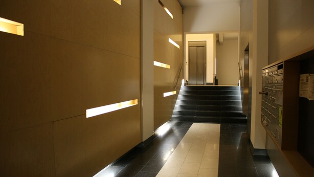 A modern interior with a staircase leading to an elevator, a reception desk, and a wall-mounted storage unit. - Luxury Oldtown Apartments (Vienna)
