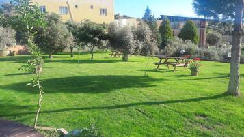 Un jardín bien cuidado con una mesa de picnic, plantas en macetas y un edificio amarillo al fondo.