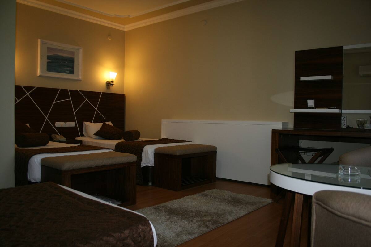 Habitación de hotel con dos camas, una mesita, una silla, un sofá, un espejo y un televisor instalado en la pared.