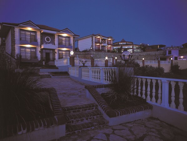 A multi-story residential building with a stone facade, multiple balconies, and a well-lit entrance.