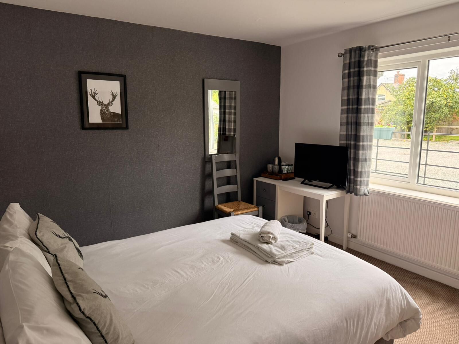 A bedroom with a bed, a desk with a TV, a chair, a window with curtains, and a picture on the wall.