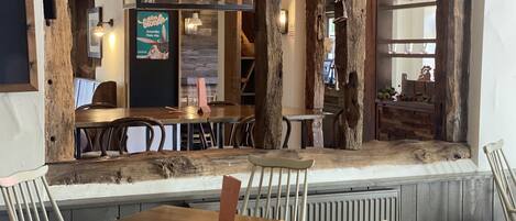 A rustic interior with wooden beams, metal watering cans, a wooden table, and chairs.