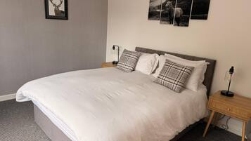 A neatly made bed with a grey headboard, a bedside table with a lamp, and a framed picture of a deer on the wall.