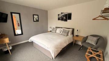 A bedroom with a large bed, a bedside table, a chair, and a wall-mounted TV.