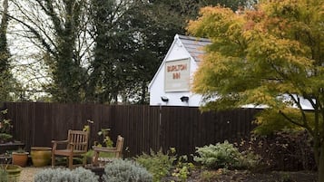 A white building with a sign reading "Burlton Inn" in a garden setting with a wooden fence, potted plants, and a bench.