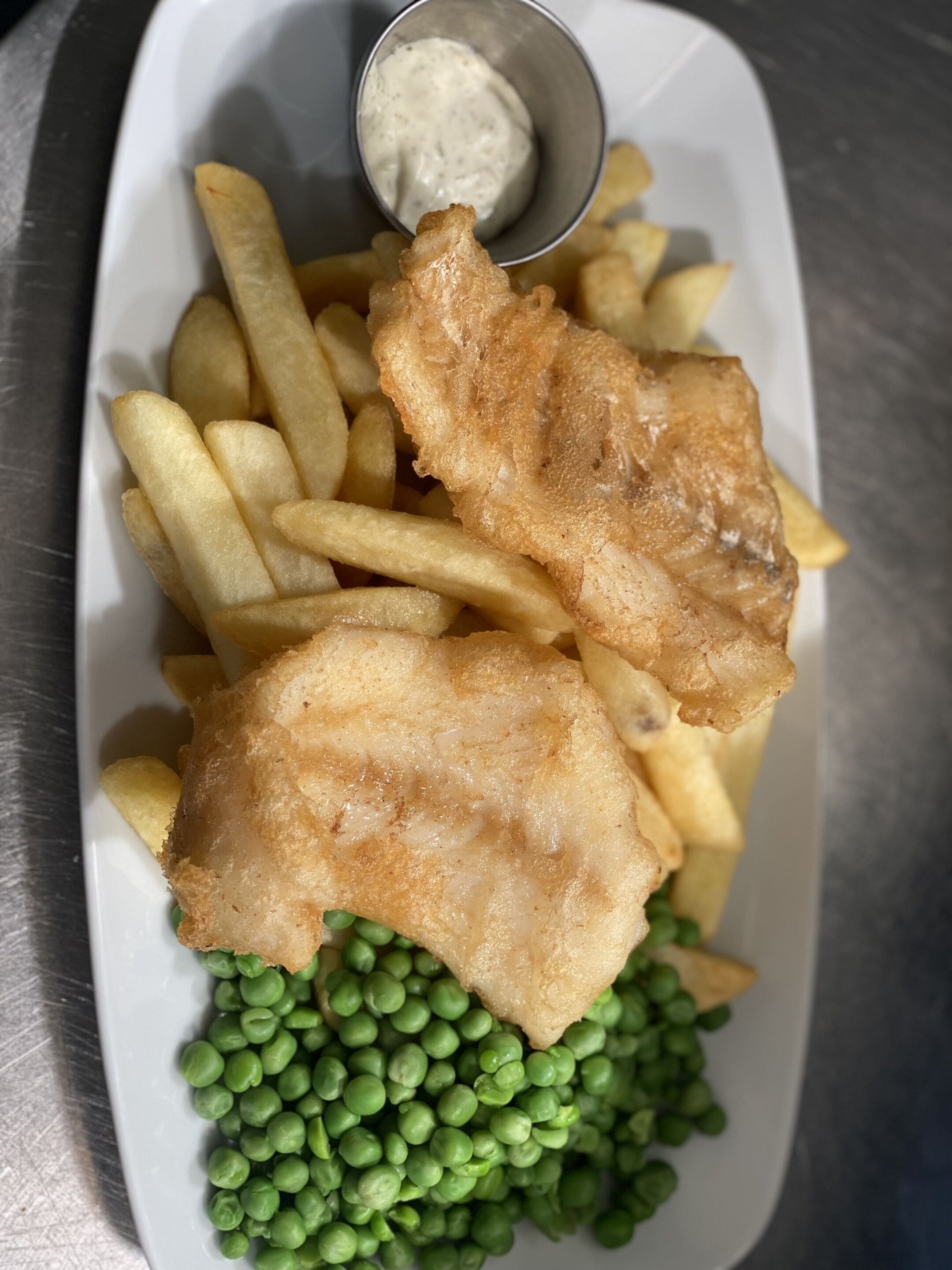 A plate with fish and chips, peas, and a small bowl of sauce.
