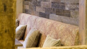 A wooden bench with a cushion and a stone wall in the background.