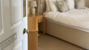 A bedroom with a bed, nightstand, and a door labeled "FENEMERE".