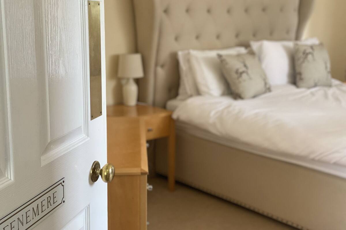 A bedroom with a bed, nightstand, and a door labeled "FENEMERE".