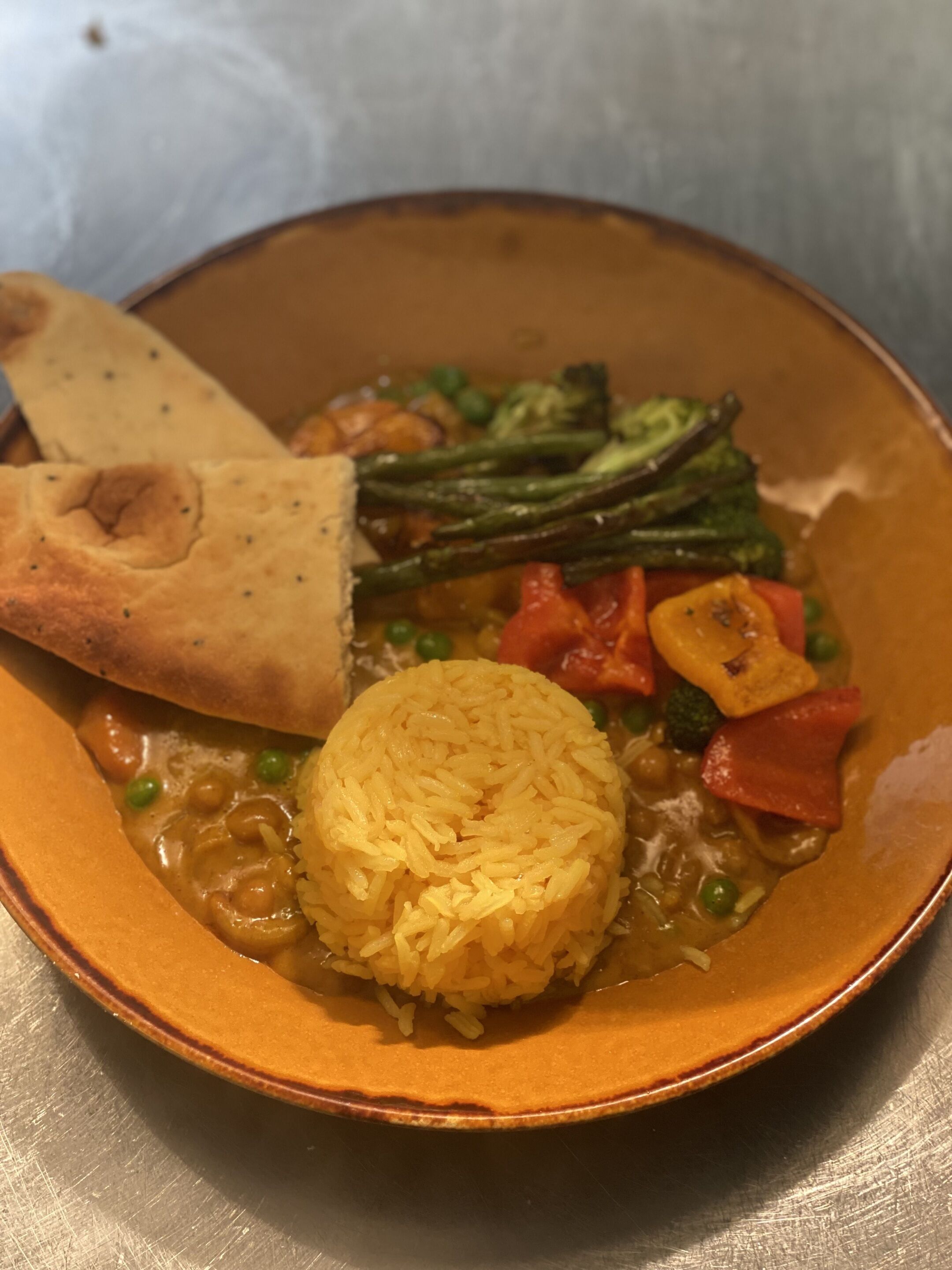 A bowl of food with rice, vegetables, and a piece of flatbread.