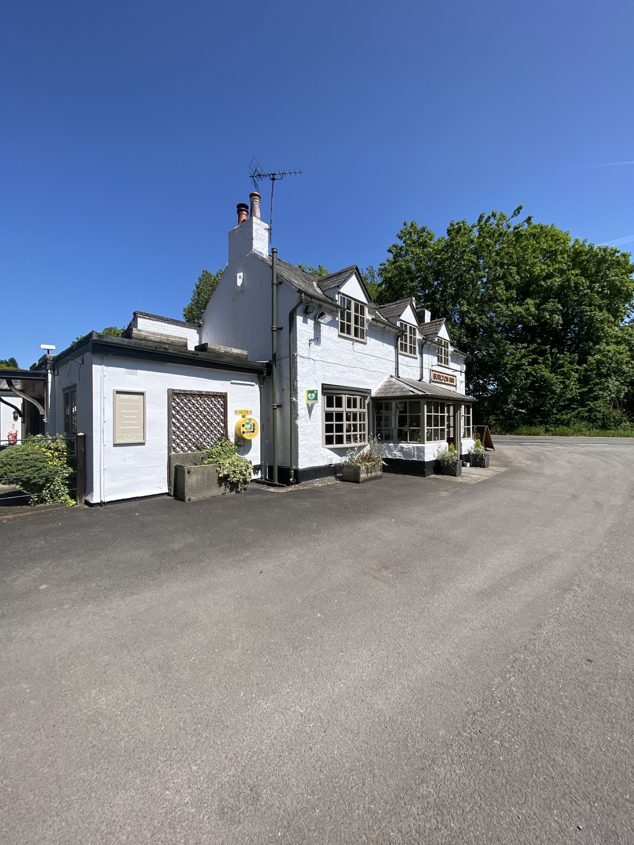 A white building with a chimney, a signboard, and a small garden area.