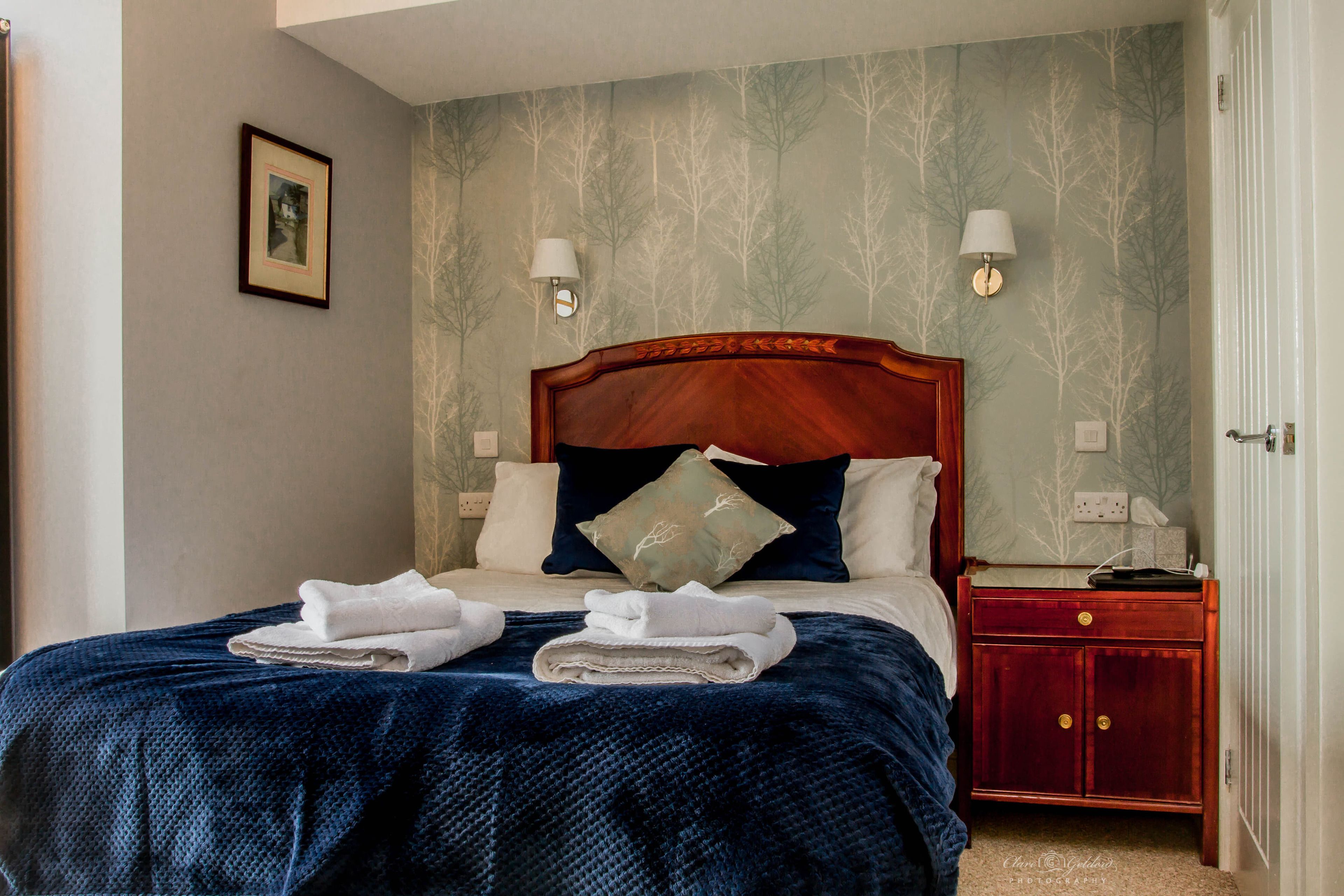 A neatly made bed with a dark blue blanket, a wooden headboard, and two bedside lamps.