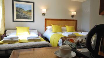 Habitación de hotel con dos camas, cada una con almohadas amarillas y ropa de cama blanca, un cuadro de paisaje enmarcado en la pared, y una mesa con una taza y un platillo.