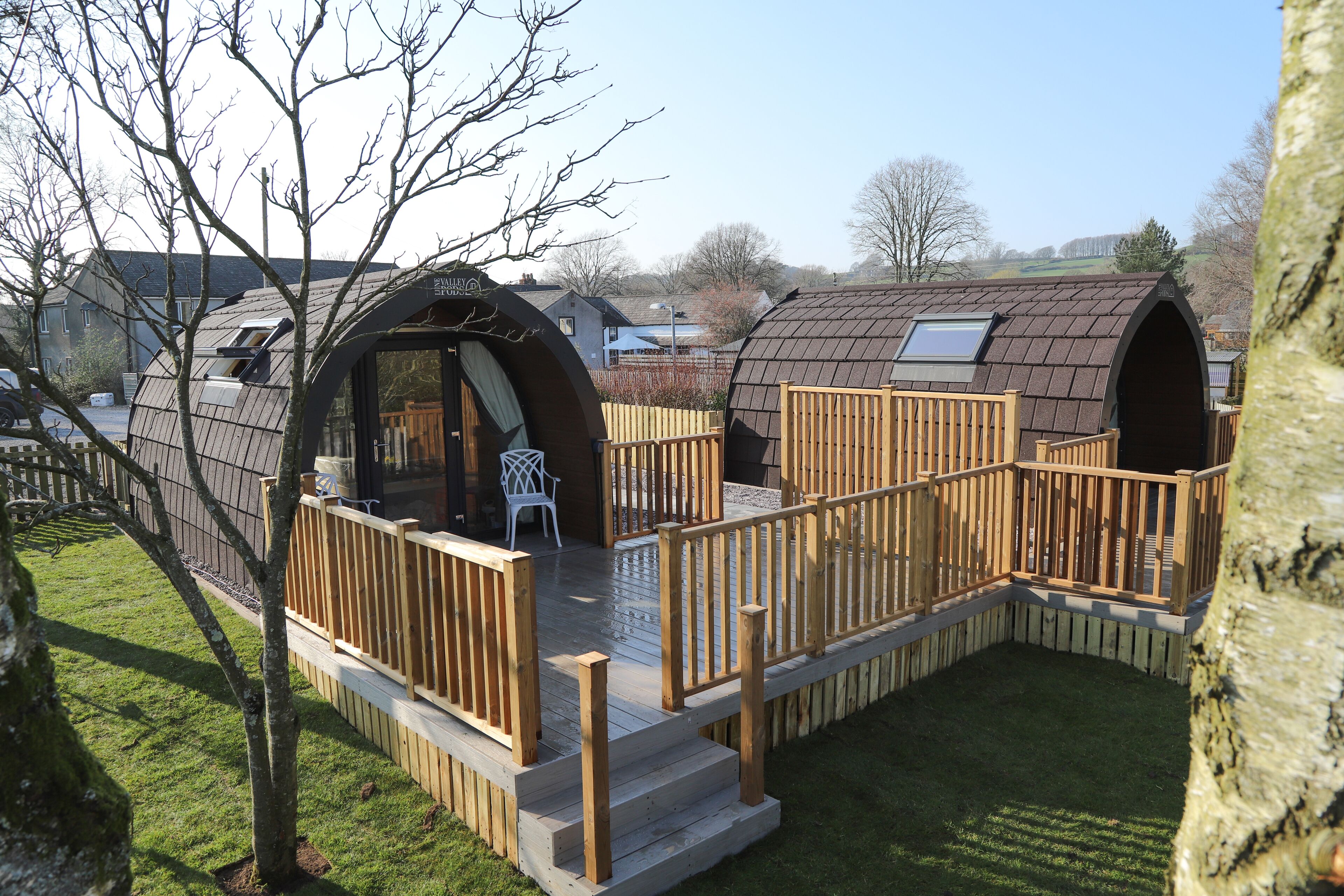 Une petite structure en bois fermée, dotée d’une terrasse et d’une fenêtre, entourée d’une clôture en bois et d’une zone herbeuse.