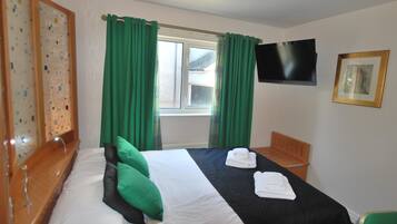 Een hotelkamer met een bed, groene gordijnen, een televisie en een ingelijste foto aan de muur.