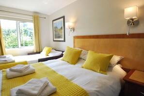 A hotel room with two beds, each with yellow and white bedding, and a large window providing a view of greenery.