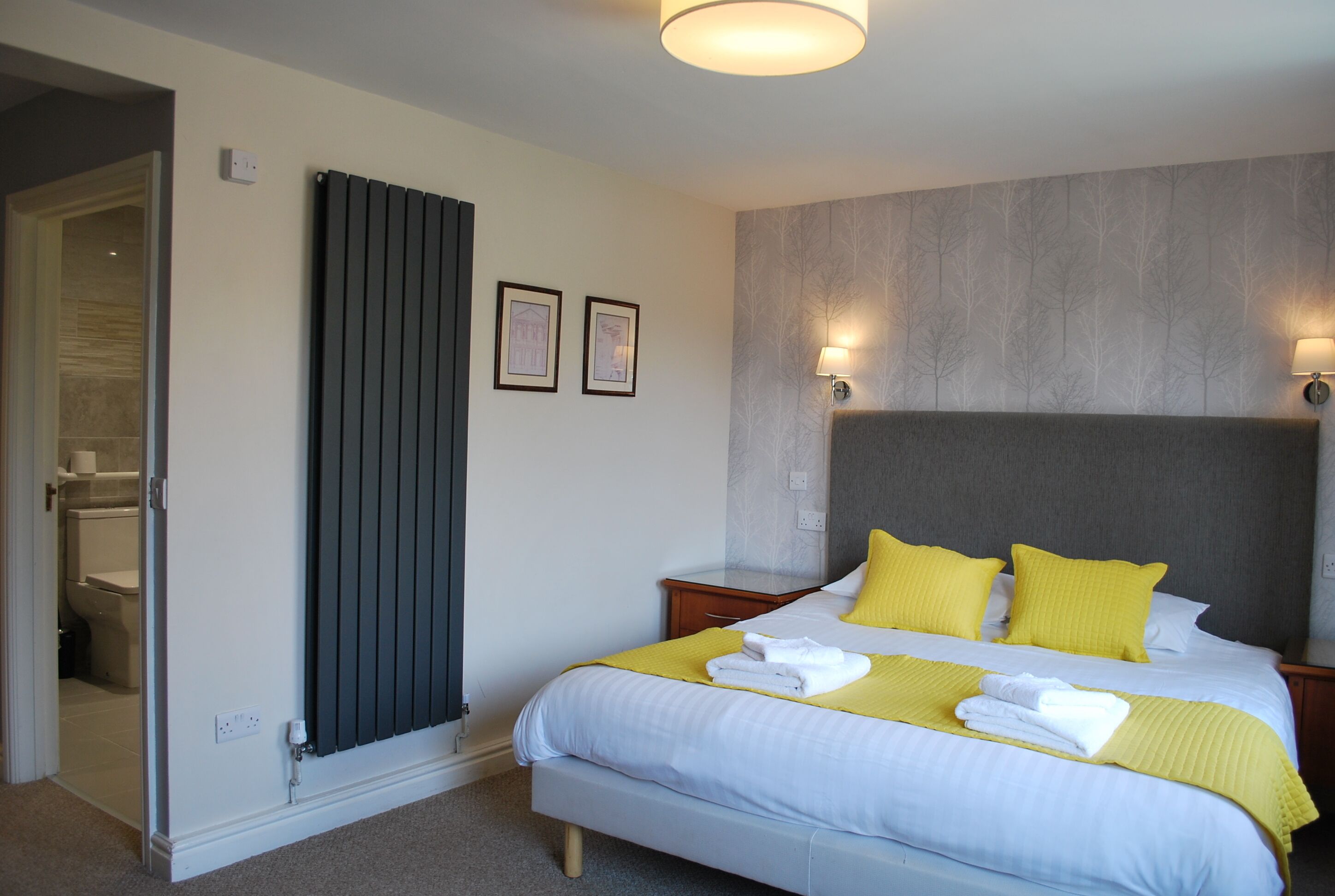 A hotel room with a bed, bedside lamps, a radiator, and a bathroom visible through an open door.