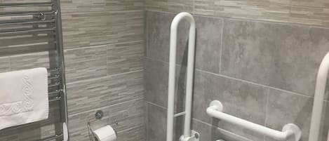 A modern bathroom with a toilet, grab bars, a towel rack, and a trash bin.