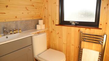 A compact wooden bathroom with a toilet, sink, and window.
