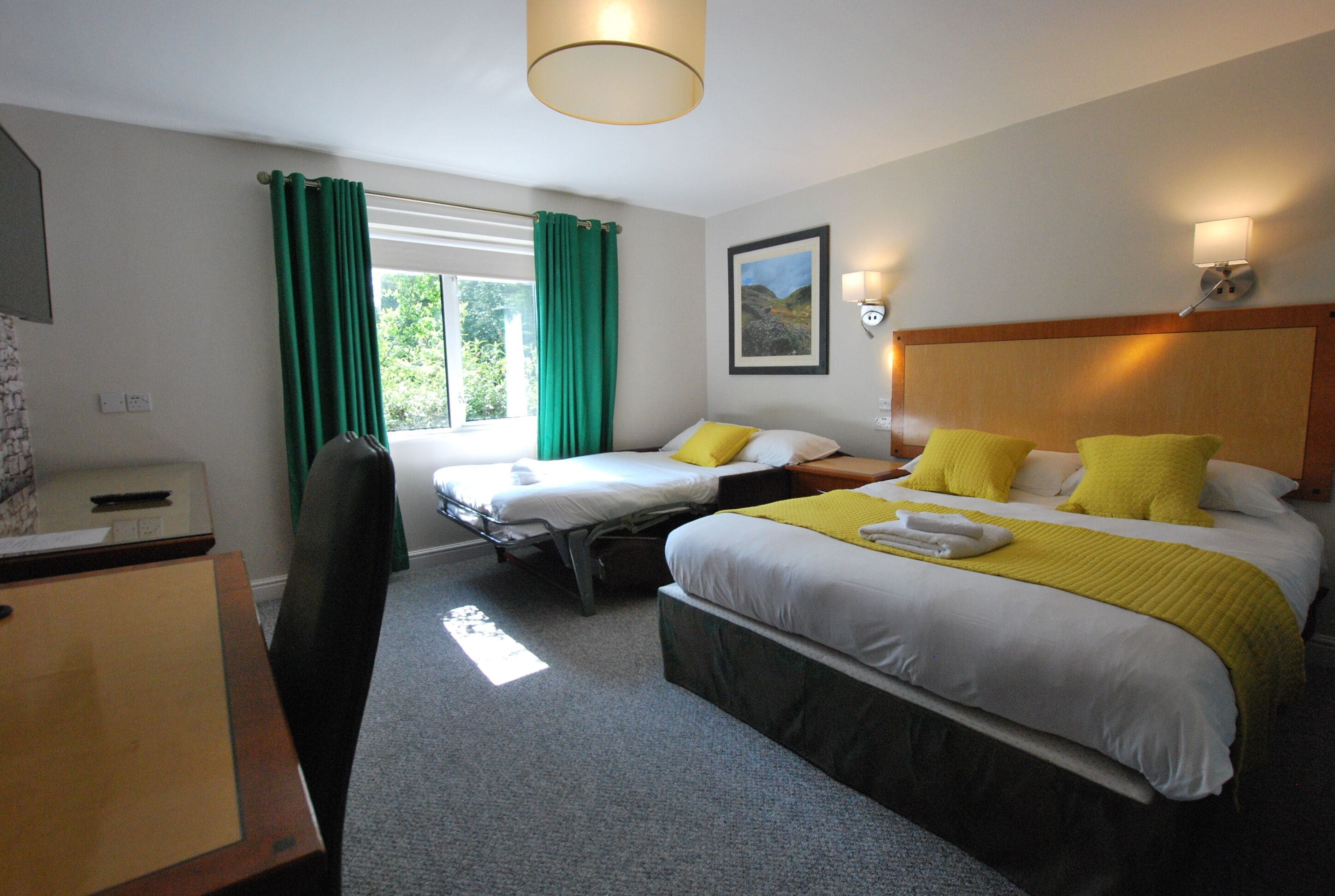 A hotel room with two beds, a desk, a chair, a window with curtains, and a picture on the wall.